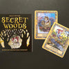 A box labeled Secret Woods by Schiffer Publishing, Ltd. sits on a dark surface next to two illustrated cards—Collector with a badger and Messenger with a fox on a bicycle—from this enchanting intuition card deck.