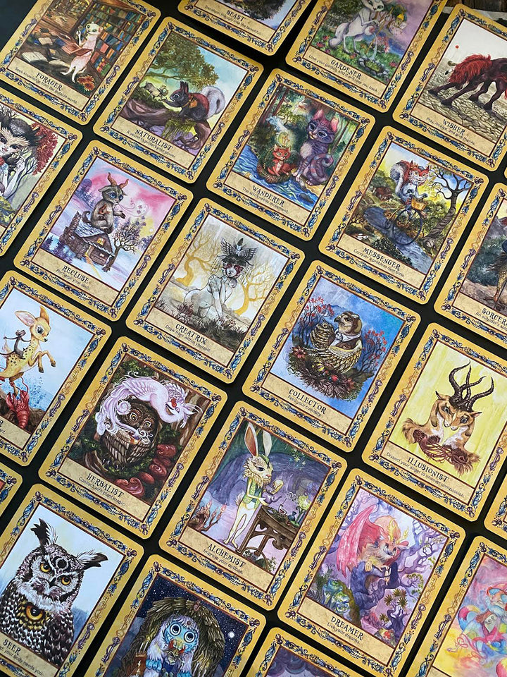 Secret Woods by Schiffer Publishing, Ltd. features illustrated intuition cards with whimsical animals, fantasy creatures, and mystical scenes—each bordered in gold with distinct labels and intricate artwork arranged on a surface.