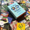 A vibrant array of tarot and divination cards encircles the light blue La Santa Muerte Lenormand box by Schiffer Publishing, Ltd., a deck featuring detailed illustrations, numbers, and suit symbols.
