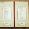 The Herbarium of Fabric Flowers by Schiffer Publishing, Ltd. lies open on a wooden table, showing its table of contents on textured cream pages with a gold clasp and two small cards at the bottom—ideal for herbarium fabric projects.