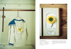 A white sailor-style shirt with blue trim, adorned by a yellow ranunculus, exemplifies wearable plant art. Nearby is "The Herbarium of Fabric Flowers" by Schiffer Publishing, Ltd., echoing the theme of herbarium fabric projects.