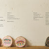 Four colorful hoops with detailed botanical embroidery from Schiffer Publishing, Ltd.’s "Embroidery Garden" rest on wood before a beige wall. Above, a contents page lists sections and page numbers, inspired by Yanase Rei’s artistry.