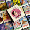 A box of Dream Your Joy Oracle Cards by Schiffer Publishing, Ltd. rests on vibrant affirmation cards, each showcasing whimsical, fantasy-inspired art and uplifting messages—ideal for dream meditation and positive inspiration.