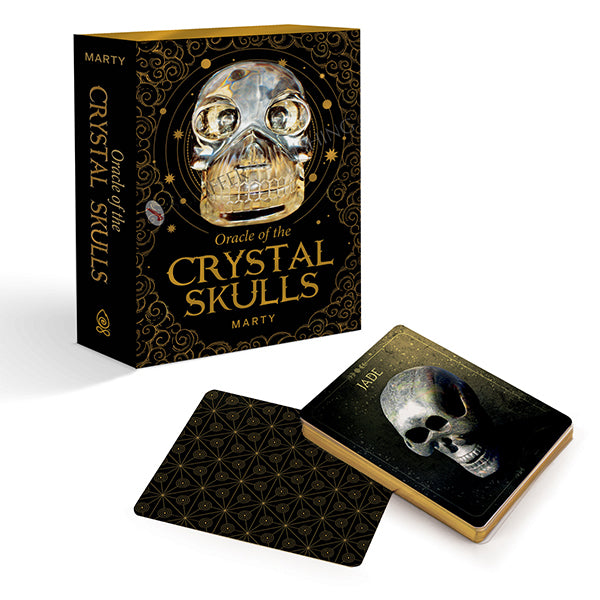 A box labeled "Oracle of the Crystal Skulls" by Schiffer Publishing, Ltd. stands upright beside its oracle deck; one card features a skull and "Jade," suggesting spiritual growth, while another displays a black-and-gold geometric design.