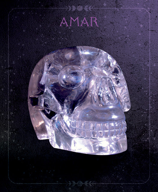 A clear crystal skull with detailed features sits against a dark, textured backdrop. The product, "Oracle of the Crystal Skulls" by Schiffer Publishing, Ltd., features the word AMAR above the skull in purple letters, inspired by oracle card art.