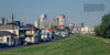 A grassy levee borders homes in the foreground, reminiscent of 1990s New Orleans scenes, with the city's modern skyline rising behind—all as featured in "New Orleans" by Schiffer Publishing, Ltd.