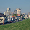 A grassy levee borders homes in the foreground, reminiscent of 1990s New Orleans scenes, with the city's modern skyline rising behind—all as featured in "New Orleans" by Schiffer Publishing, Ltd.