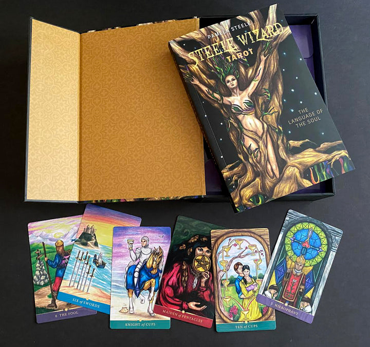 The Steele Wizard Tarot by Schiffer Publishing, Ltd. is shown on a black surface with its open patterned gold box, guidebook, and five illustrated cards: Six of Swords, Knight of Cups, Magician, Ten of Cups, and The Lovers.