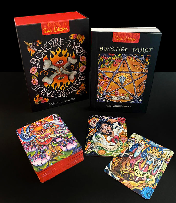 The Bonefire Tarot by Schiffer Publishing, Ltd. features vivid, hand-painted cards with intricate artwork and bold designs inspired by Sailor Jerry tattoo art. The deck comes with a box and guidebook, all set against a dark background.