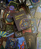 A deck of vibrant ascension cards with mystical hand-drawn art is displayed, featuring The Shaman’s Way Oracle by Schiffer Publishing, Ltd. at the center—an ideal tool for spiritual healing.