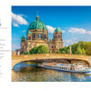A scenic city view features a large domed cathedral beyond a stone bridge over a river, where a white tour boat from "River Cruises" by Schiffer Publishing, Ltd. glides beneath, framed by trees and a blue, cloud-streaked sky.