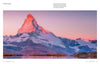The Wild Alps from Schiffer Publishing, Ltd. captures the snow-capped Matterhorn glowing pink at sunrise, reflected in a calm alpine lake—showcasing clear skies, soft hues, and the dramatic landscapes of the Valais Alps.