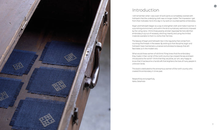 Six small square navy blue swatches with white counted sashiko embroidery from Schiffer Publishing, Ltd.’s Counted Sashiko Embroidery are arranged in an open vintage suitcase. A printed introduction and signature appear on the right.