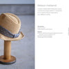 A straw hat with a wide gray ribbon band inspired by Counted Sashiko Embroidery from Schiffer Publishing, Ltd. rests on a wooden stand. Illustrated instructions and measurements for making the ribbon hatband are shown to the right.