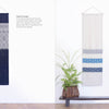 Two "Counted Sashiko Embroidery" tapestries by Schiffer Publishing, Ltd. hang above a wooden bench with potted plants—one navy with white sashiko embroidery, the other beige with blue and white striped patterns. Text describes each tapestry.
