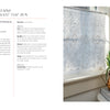 A bright, airy room features Nordic Hands by Schiffer Publishing, Ltd.—a delicate white curtain with a geometric diamond pattern inspired by Scandinavian fiber art—hung in a sunlit window beside a copper pitcher with greenery.