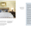 A stylish bedroom from Schiffer Publishing, Ltd.'s "It's All in the Mix" features a tufted headboard, two bedside tables with lamps, decorative pillows, patterned wallpaper, and neatly layered neutral bedding.