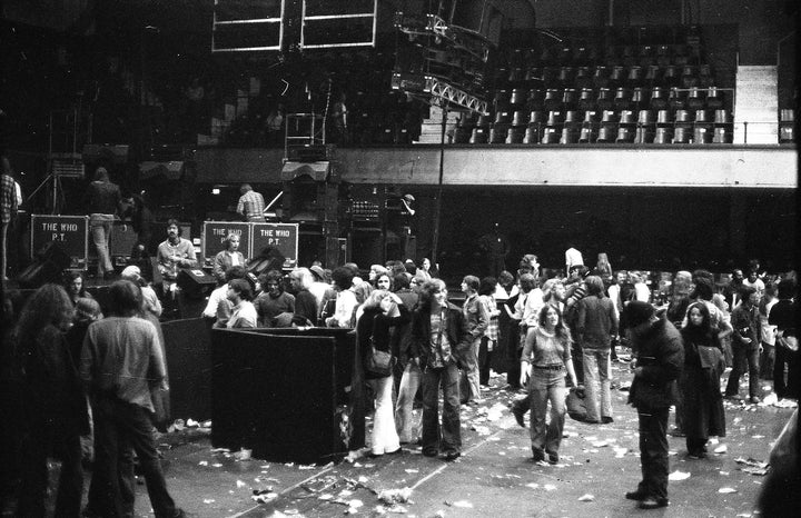 A black-and-white photo featured in "Teenage Wasteland" by Schiffer Publishing, Ltd. captures a litter-strewn indoor arena after The Who's Winterland show, with people lingering near equipment marked "The Who.