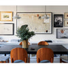 A stylish dining room inspired by *Interior Designers at Home* from Schiffer Publishing, Ltd.—featuring a black table, six cushioned wooden chairs, greenery in a vase, a gallery wall, and two pendant lights for designer-worthy ambiance.