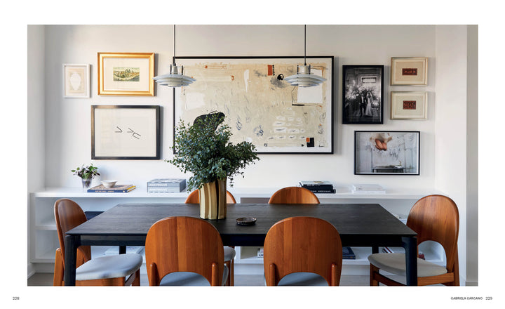 A stylish dining room inspired by *Interior Designers at Home* from Schiffer Publishing, Ltd.—featuring a black table, six cushioned wooden chairs, greenery in a vase, a gallery wall, and two pendant lights for designer-worthy ambiance.