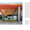 The entrance, inspired by "Innovations in Mass Timber" from Schiffer Publishing, Ltd., features geometric timber ceilings, expansive glass, and bold red-orange columns, showcasing the environmental benefits of modern commercial architecture amid urban greenery.