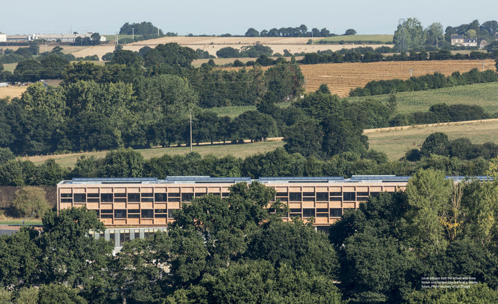 Among dense trees and rolling hills, a rectangular mass timber building with a flat roof exemplifies the environmental benefits discussed in "Innovations in Mass Timber" by Schiffer Publishing, Ltd., beneath a clear sky.