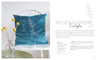 A blue velvet "Stitch with One Line" cushion by Schiffer Publishing, Ltd., featuring a white one-line eucalyptus embroidery, rests on a white chair beside a vase of yellow billy balls. Text to the right details the cushion and its materials.