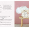 The book "Stitch with One Line" by Schiffer Publishing, Ltd. is displayed on a light wooden surface against a pink wall, accompanied by a canvas bunny basket filled with fluffy white material and embroidery project tips.