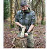 A man in green plaid kneels in a forest, splitting a log on a stump with a knife—practicing bushcraft skills just like those taught in "Core Bushcraft" by Schiffer Publishing, Ltd., for the authentic outdoor survival experience.
