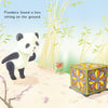 A cute panda stands on a bamboo path, gazing at a colorful box. Text: Pandora found a box on the ground. The Magic Box by Schiffer Publishing, Ltd. is perfect for emerging readers and a delightful panda children’s book adventure.