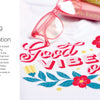 A close-up of a white cloth made with Sublimation Crafting by Schiffer Publishing, Ltd. displays colorful "Good Vibes Only" text with floral designs. Pink-rimmed glasses and vibrant books appear partly in the background.
