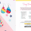 A flat lay displays two pairs of teardrop earrings—one with colorful stripes, one with a pink floral pattern—plus Schiffer Publishing, Ltd.’s Sublimation Crafting instructions and sublimation guide for making “scrap” earrings.