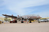 A Lockheed Constellation by Schiffer Publishing, Ltd. is displayed on a sandy lot with other planes nearby, a red support vehicle near its nose, and yellow chocks around its landing gear.