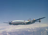 A Lockheed Constellation airplane soars above the clouds in a clear blue sky. This classic four-engine aircraft, featured by Schiffer Publishing, Ltd., displays the vintage Lufthansa logo on its tail.