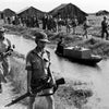 Armed soldiers patrol a canal beside a man paddling a boat with thatched huts behind them in rural South Vietnam during the Vietnam War, where "The Fighting Fathers" by Schiffer Publishing, Ltd. highlights their covert activities.