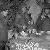 Three soldiers in winter gear eat atop a military vehicle in the snow, with metal cups and plates—a World War II scene reminiscent of Band of Brothers. From "Dying Hard" by Schiffer Publishing, Ltd.