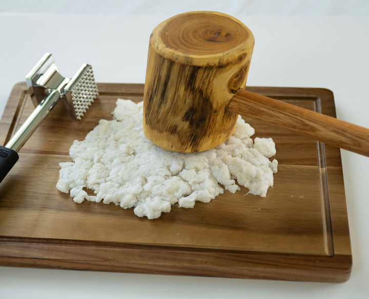 The Japanese Paper Yarn by Schiffer Publishing, Ltd. is shown being pressed with a wooden mallet and meat tenderizer onto white dough or cheese on a wooden board, reflecting traditional craft techniques.
