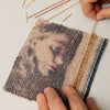A person inserts thin wooden sticks into a textile square made with Schiffer Publishing, Ltd. Japanese Paper Yarn, featuring a muted image of a woman’s profile, as hands and sticks rest on a white surface.