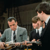 Capturing Beatlemania, Schiffer Publishing, Ltd.’s The Beatles in America features a man in a gray suit examining a guitar as The Beatles watch and smile in what appears to be a studio or rehearsal space.