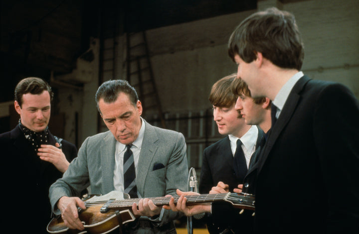 Capturing Beatlemania, Schiffer Publishing, Ltd.’s The Beatles in America features a man in a gray suit examining a guitar as The Beatles watch and smile in what appears to be a studio or rehearsal space.