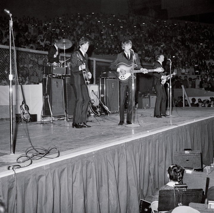 A black and white photo in Schiffer Publishing, Ltd.'s "The Beatles in America" captures the band's energetic stadium performance, with amplifiers, guitars, and cheering floor-to-stand crowds visible.