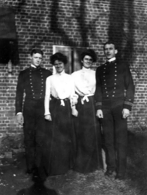 Four people pose outside a brick building: two men in military-style uniforms and two women in skirts and blouses. The black and white image evokes US Navy history, echoing the spirit of "King's Navy" by Schiffer Publishing, Ltd.
