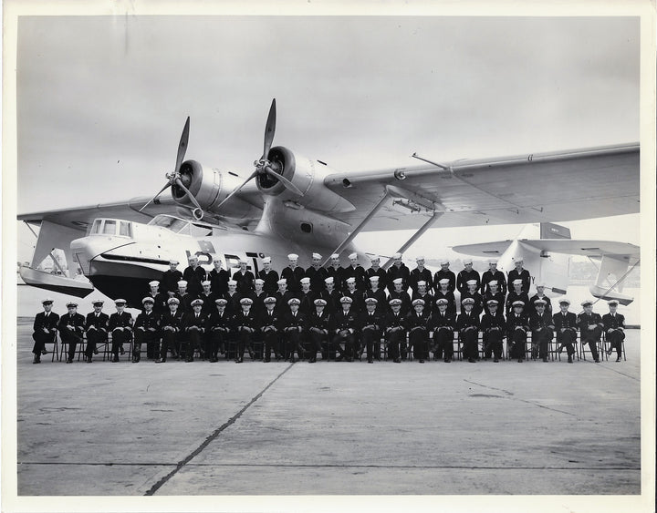 A large group of uniformed personnel poses before a twin-engine seaplane, reflecting US Navy history—an image featured in King's Navy by Schiffer Publishing, Ltd. The group gathers on the tarmac beneath the plane's wings and propellers.