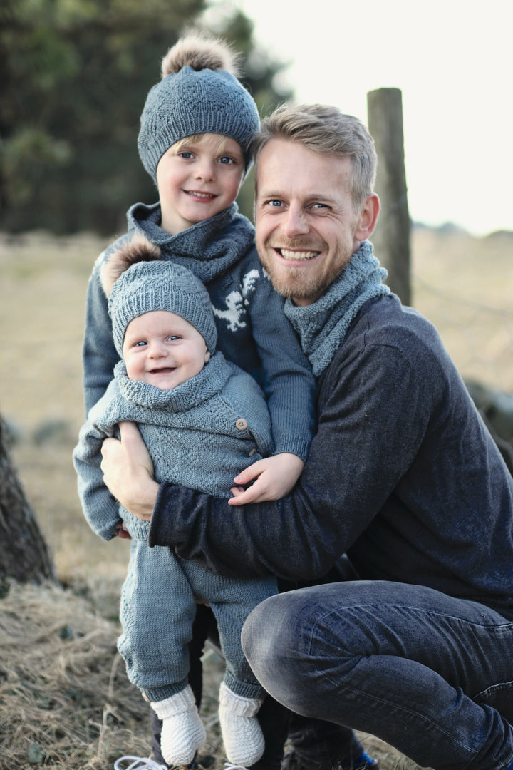 A man hugs two children outdoors, all in matching blue outfits inspired by "Winter Knitting for Little Sweethearts" from Schiffer Publishing, Ltd., perfect for a chilly day that highlights cozy Nordic design and style.