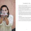 A woman blows confetti in the air, surrounded by Magical Crochet accessories from Schiffer Publishing, Ltd., adding a whimsical touch to her joyful moment.