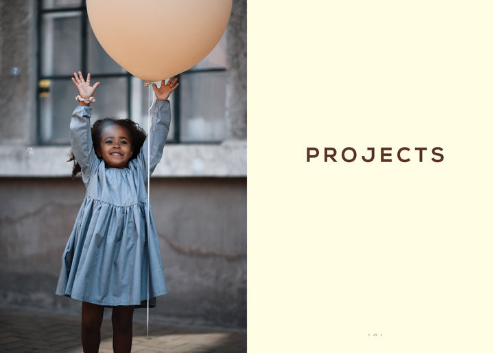 A young girl in a blue dress smiles, holding a large orange balloon against an urban backdrop with "PROJECTS" on a cream panel, inviting kids to explore Schiffer Publishing, Ltd.'s Magical Crochet for imaginative patterns and fun accessories.
