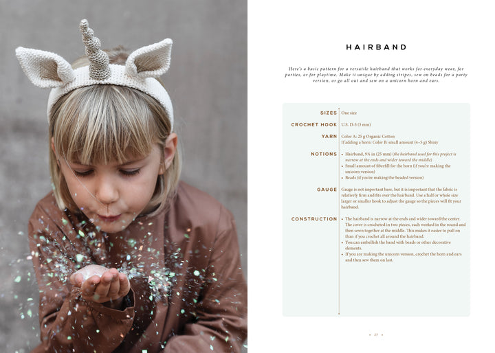 A young child with light hair, wearing a brown jacket and the Magical Crochet unicorn headband from Schiffer Publishing, Ltd., blows glitter into the air against a soft, neutral background.