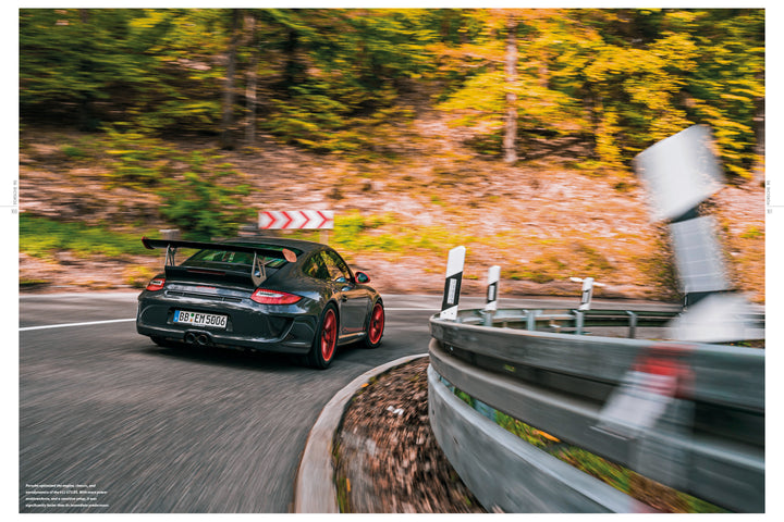 The Porsche RS by Schiffer Publishing, Ltd. speeds around a mountain curve, its black exterior and red wheels accentuated by autumn trees and blurred guardrails, capturing its thrilling Renn Sport legacy in motion.