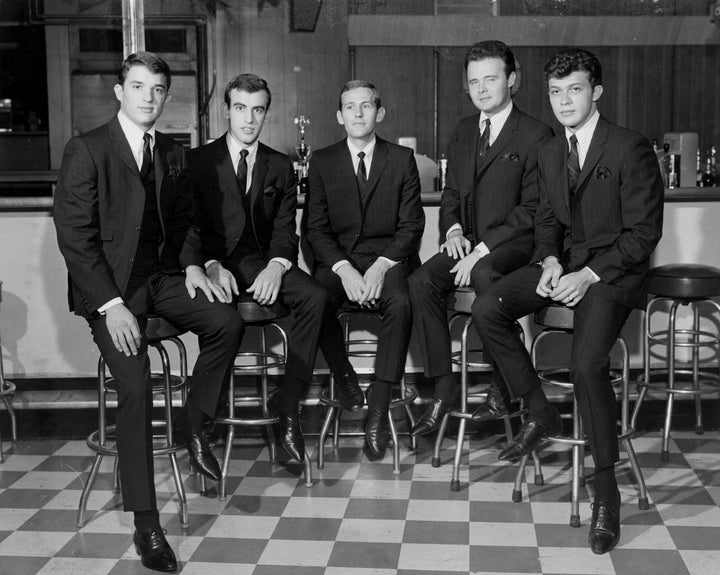 Five men in dark suits and ties sit on bar stools at a counter in a retro-style setting with a checkered floor, evoking the timeless atmosphere featured in Schiffer Publishing’s Richard Manuel.