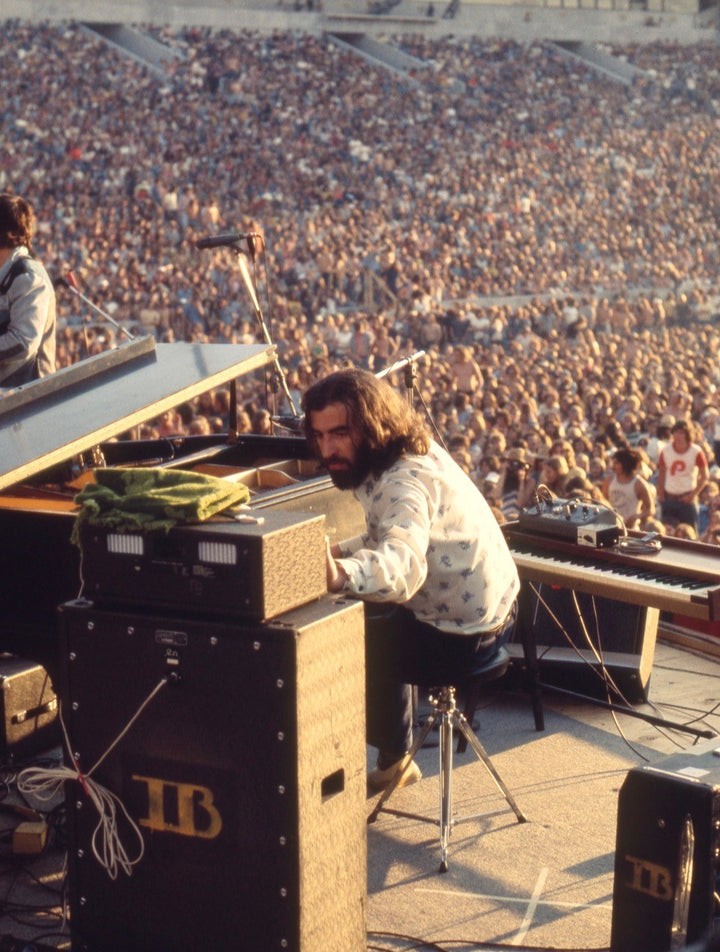 A musician reminiscent of Richard Manuel performs on keyboards at an outdoor stadium concert before a large crowd, capturing classic rock vibes. Sound equipment and cables are visible in the foreground. Brand: Schiffer Publishing, Ltd.
